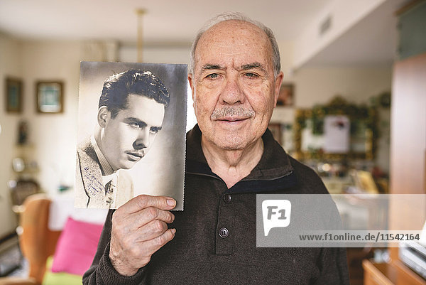 Portrait of senior man showing an old picture of himself