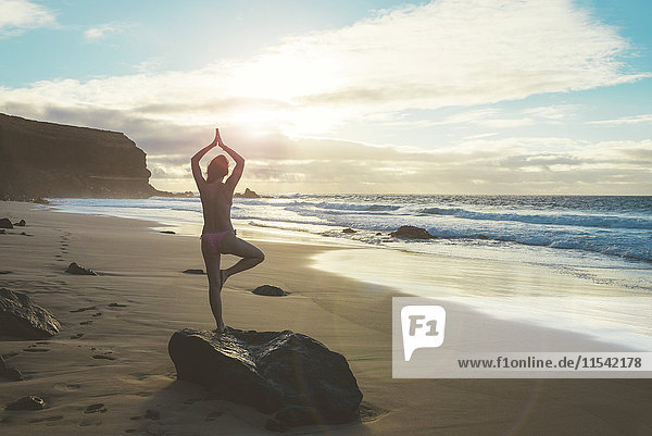 Spanien  Fuerteventura  El Cotillo  Rückansicht der Frau beim Yoga am Strand bei Sonnenuntergang