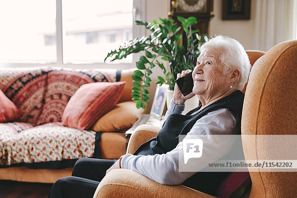 Lächelnde Seniorin beim Telefonieren mit dem Smartphone zu Hause