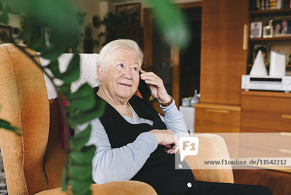 Porträt einer lächelnden Seniorin beim Telefonieren mit dem Smartphone zu Hause