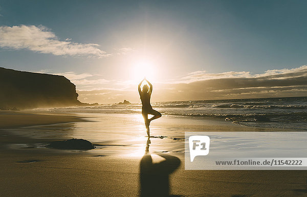 Frau beim Yoga am Strand bei Sonnenuntergang