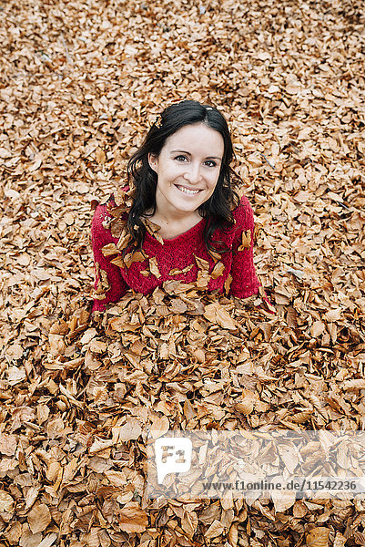 Porträt einer lächelnden Frau  die auf einem mit Herbstblättern bedeckten Waldboden sitzt.