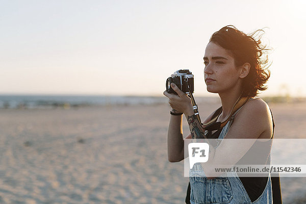 USA  New York  Coney Island  junge Frau beim Fotografieren am Strand bei Sonnenuntergang