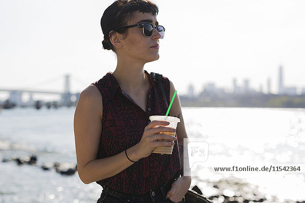 USA  New York City  Porträt einer jungen Frau mit Sonnenbrille und Plastikbecher