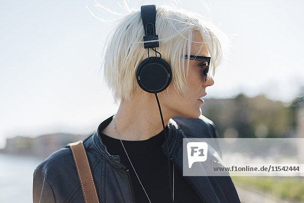 Profil der blonden Frau mit Sonnenbrille beim Musikhören mit Kopfhörer