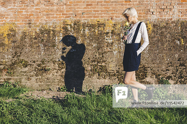 Blond woman with rose walking along a brick wall