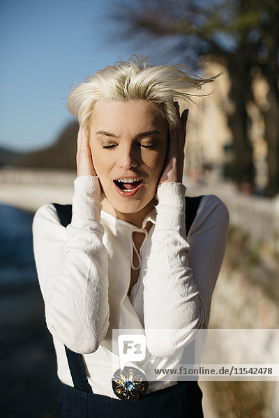 Italien  Verona  Porträt einer blonden Frau mit geschlossenen Augen und geöffnetem Mund  die die Ohren mit den Händen bedeckt.