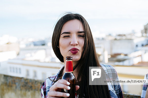 Spanien  Jerez de la Frontera  Porträt einer zwinkernden jungen Frau mit Bierflasche und schmollendem Mund
