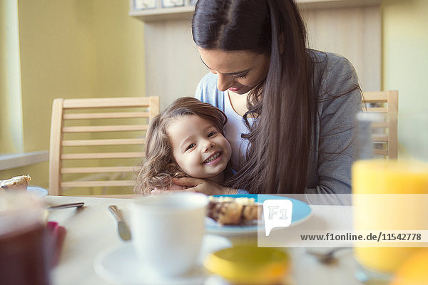 Porträt des lächelnden Mädchens und ihrer Mutter am Frühstückstisch