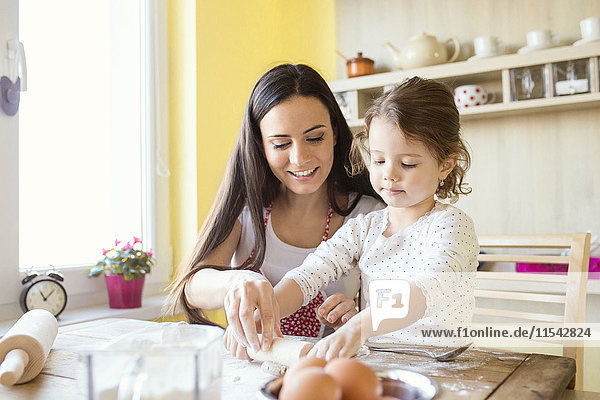 Porträt eines kleinen Mädchens und ihrer Mutter  die zusammen auf dem Küchentisch Teig ausrollen.