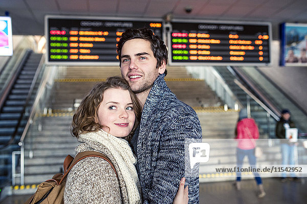 Smiling young couple embracing in station concourse