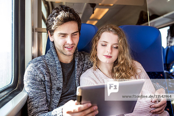 Lächelndes junges Paar im Zugwagen mit digitalem Tablett