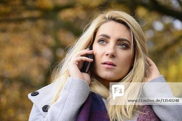 Portrait einer jungen Frau im Herbst beim Telefonieren mit dem Smartphone