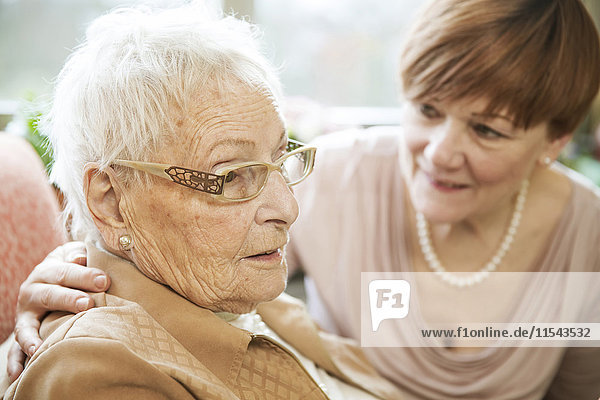 Porträt einer älteren Frau mit Alzheimer-Krankheit mit ihrer erwachsenen Tochter im Hintergrund