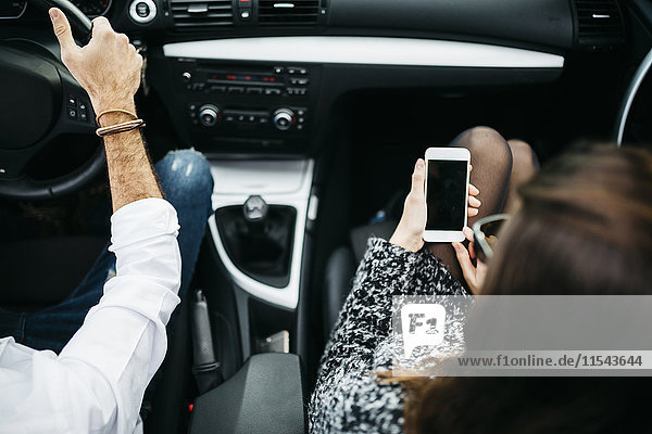 Junges Paar beim Autofahren  Beifahrer mit Smartphone