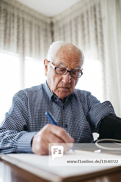 Ein älterer Mann  der seinen Blutdruck kontrolliert und das Ergebnis aufschreibt.