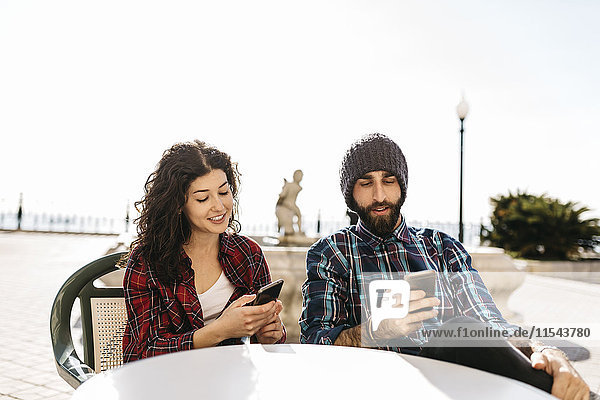 Junge Paare  die ihre Handys in einem Straßencafé benutzen.