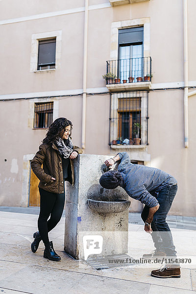 Spanien  Tarragona  Junges Paar  Mann trinkt aus Trinkbrunnen