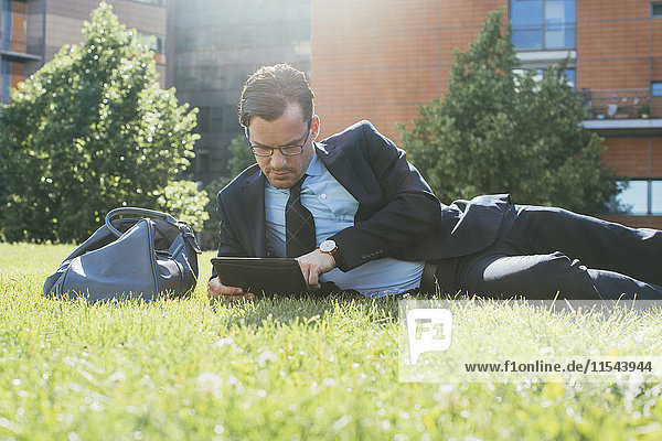 Businessman resting on meadow looking at digital tablet