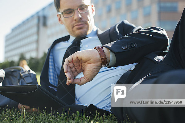 Businessman resting on meadow with digital tablet checking the time