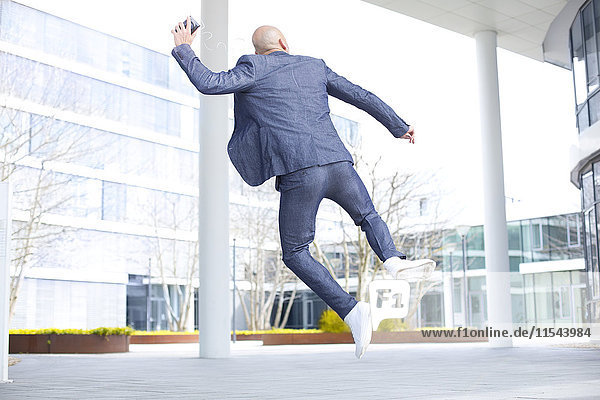 Enthusiastic businessman listening to music from smartphone and jumping mid-air