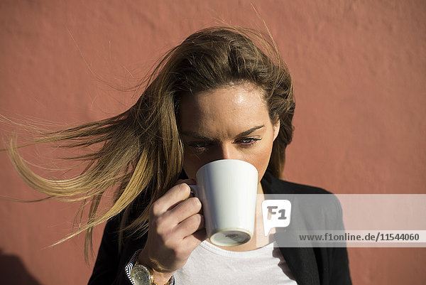 Woman with blowing hair drinking coffee
