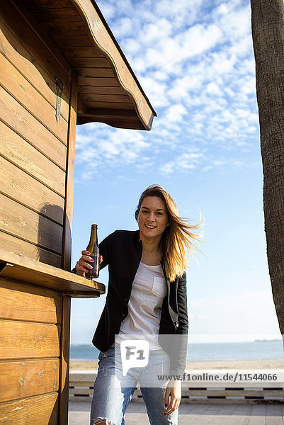 Spanien  Puerto Real  Porträt einer entspannten Frau mit Bierflasche neben einer Strandhütte