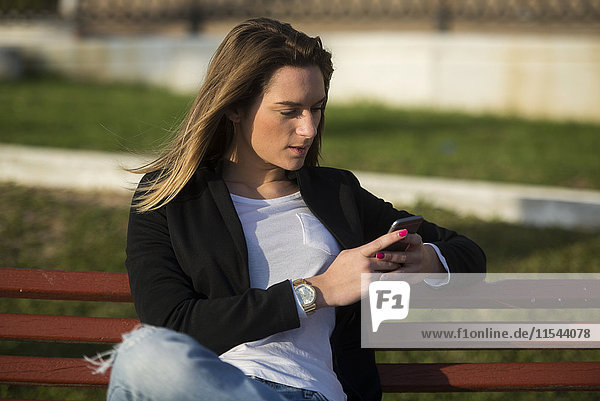 Frau sitzt auf einer Bank und schaut auf das Smartphone.