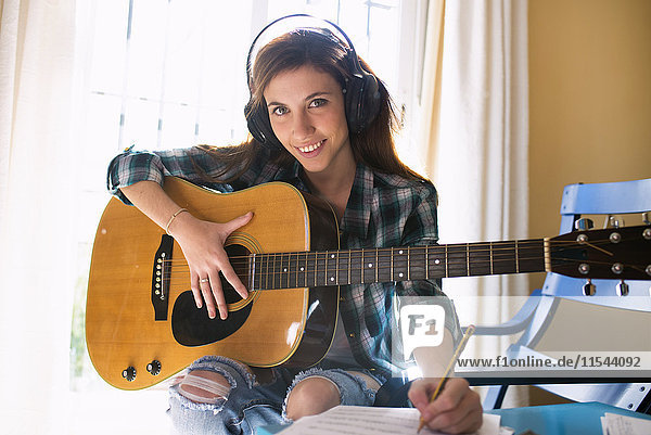 Lächelnde junge Frau mit Kopfhörer  Gitarre und Notenblatt