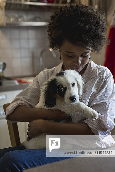 Junge Frau sitzend mit Hund auf dem Schoß in der Küche