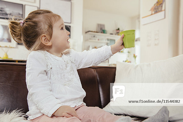 Little girl holding up a plastic cup while sitting on couch