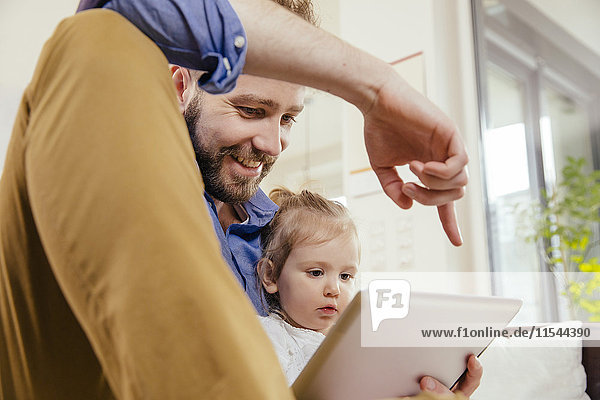 Vater zeigt seiner kleinen Tochter etwas auf digitalem Tablett