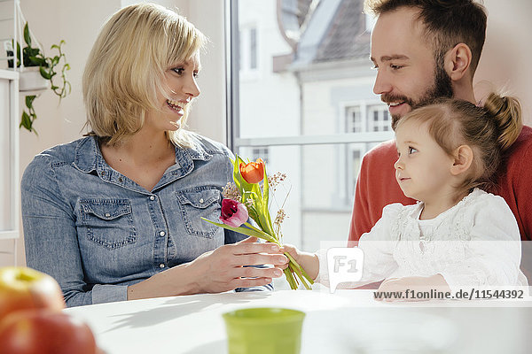 Little girl giving her mother flowers while father is watching