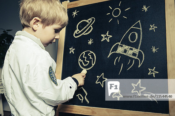 Kind mit Astronautenanzug zeichnet Himmelskörper und Leuchten auf eine Tafel