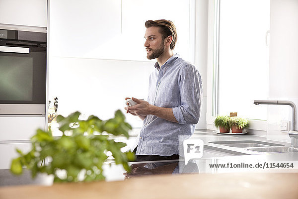Nachdenklicher junger Mann mit einer Tasse Kaffee in seiner Küche.