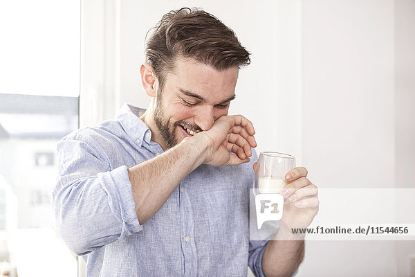 Lachender junger Mann mit einem Glas Milch  der sich den Mund wischt.