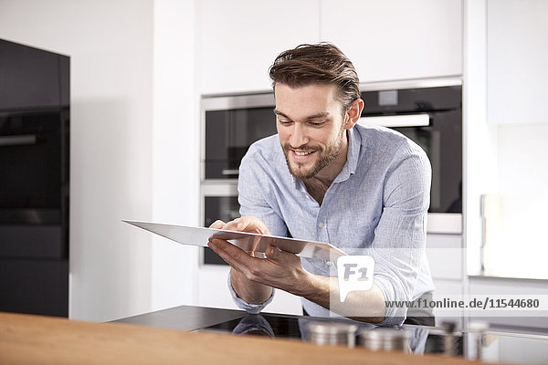 Porträt eines lächelnden jungen Mannes mit digitalem Tablett in der Küche