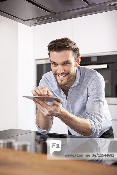 Porträt eines lächelnden jungen Mannes mit Mini-Tablette in der Küche