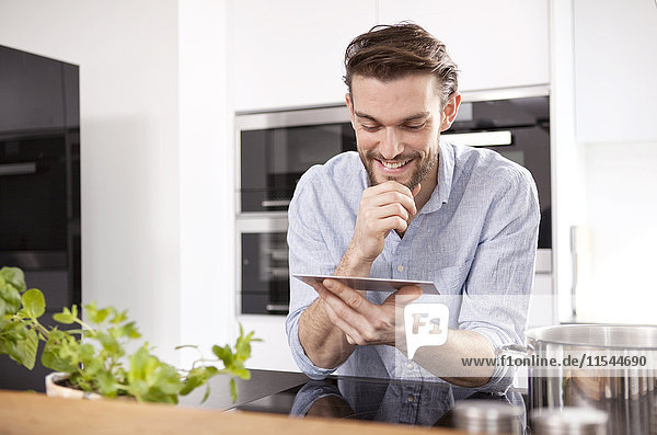 Porträt eines lächelnden jungen Mannes mit Mini-Tablette in der Küche