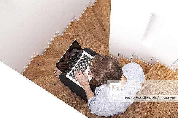 Mann auf Holztreppe sitzend mit Laptop