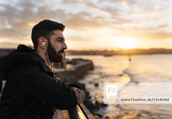 Spain  Gijon  bearded man listening music with earphones at sunset