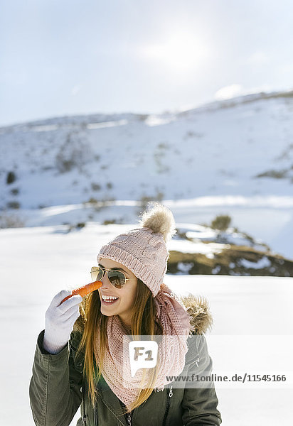 Spanien  Asturien  glückliche junge Frau mit Karotte in verschneiten Bergen