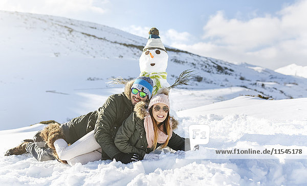 Spain  Asturias  happy couple lying in snow next to snowman