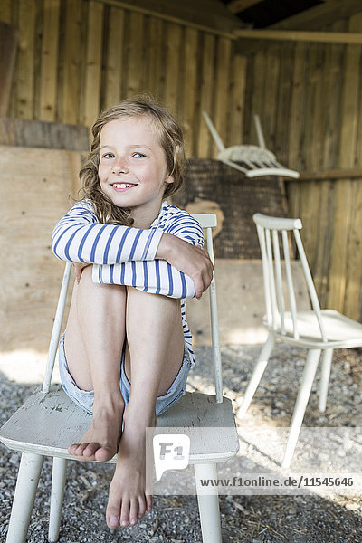 Porträt eines lächelnden blonden Mädchens  das auf einem Holzstuhl sitzt