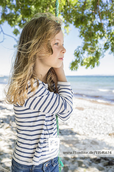 Porträt eines blonden Mädchens  das auf einer Schaukel am Strand steht