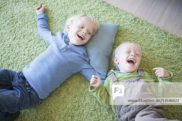 zwei lachende kleine Brüder  die zu Hause auf dem grünen Teppich liegen.