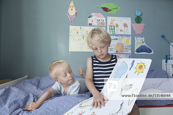 Zwei kleine Brüder auf dem Bett im Kinderzimmer beim Betrachten des Bilderbuches