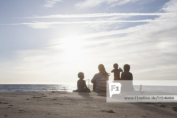 Rückansicht der Familie mit zwei Kindern am Strand bei Dämmerung