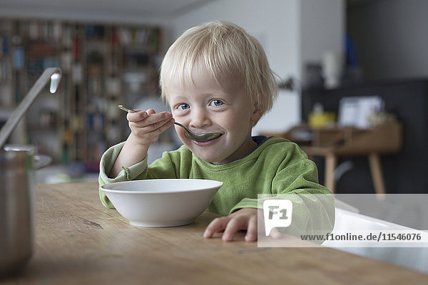 Portrait of smiling little boy eating soup at home
