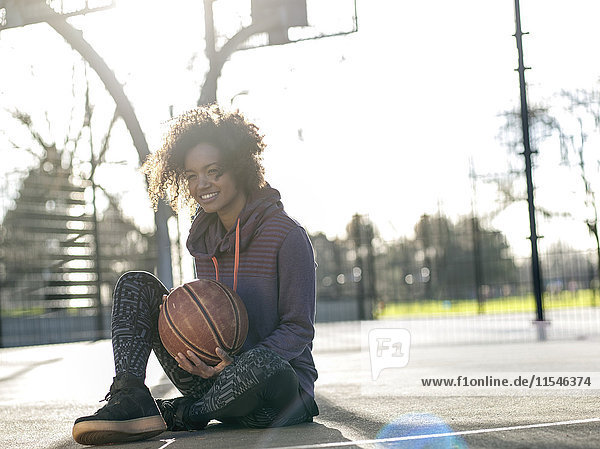 Porträt einer lächelnden jungen Frau mit Basketball auf dem Spielfeld